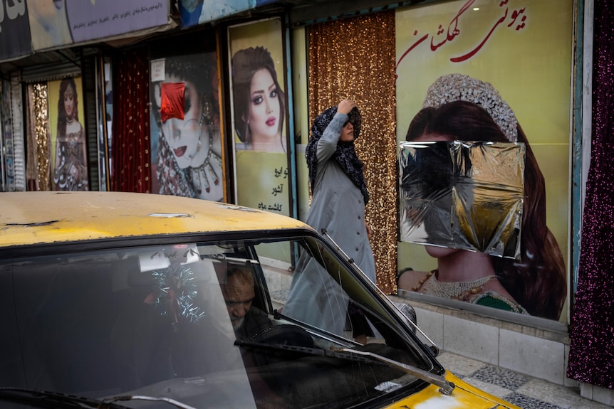 An Afghan woman walks past beauty salons with defaced window decorations