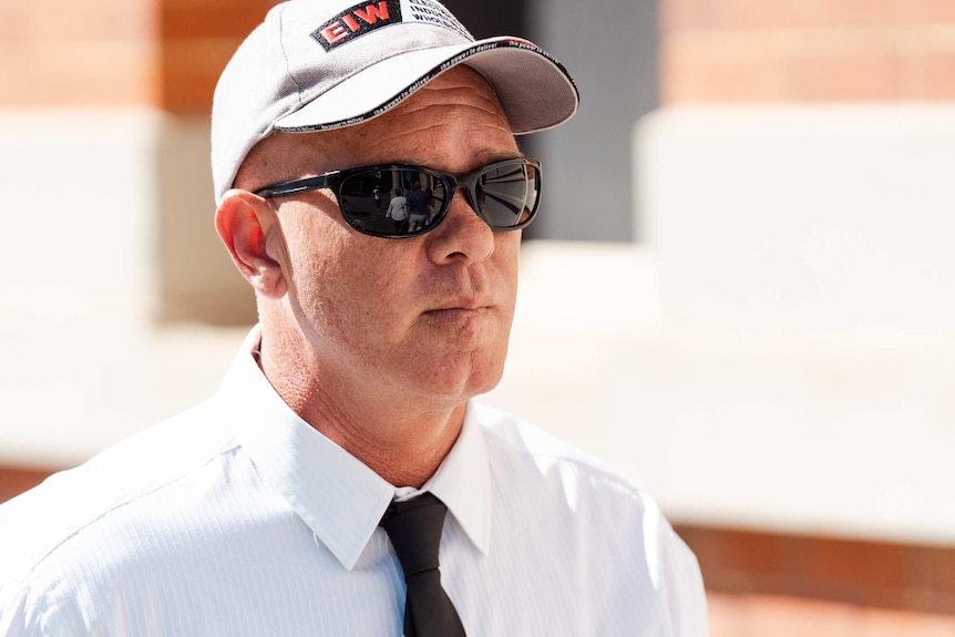 A head and shoulders shot of a man wearing a baseball cap and sunglasses