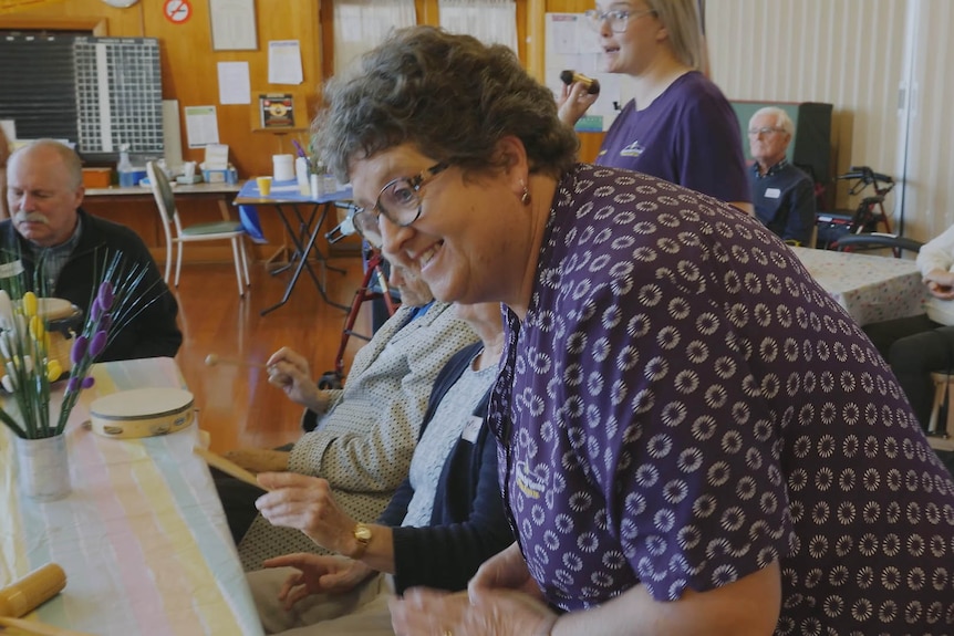 A woman leans over a table to laugh and chat.