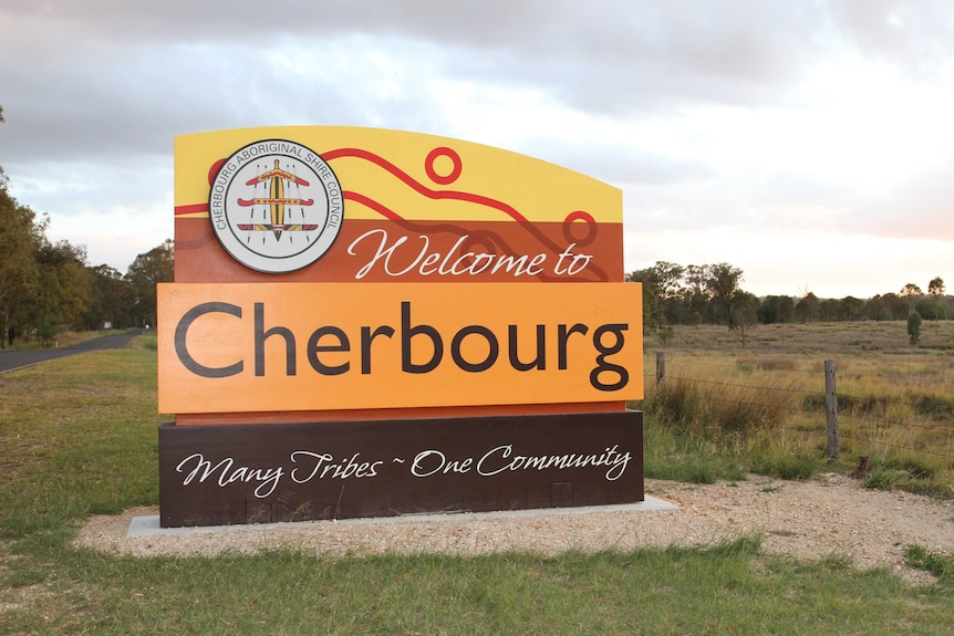 A sign stands by the side of a country road, with text reading: Welcome to Cherbourg. Many tribes - one community.