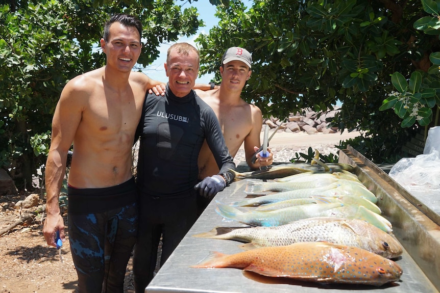 Thee men standing together with a catch of fish