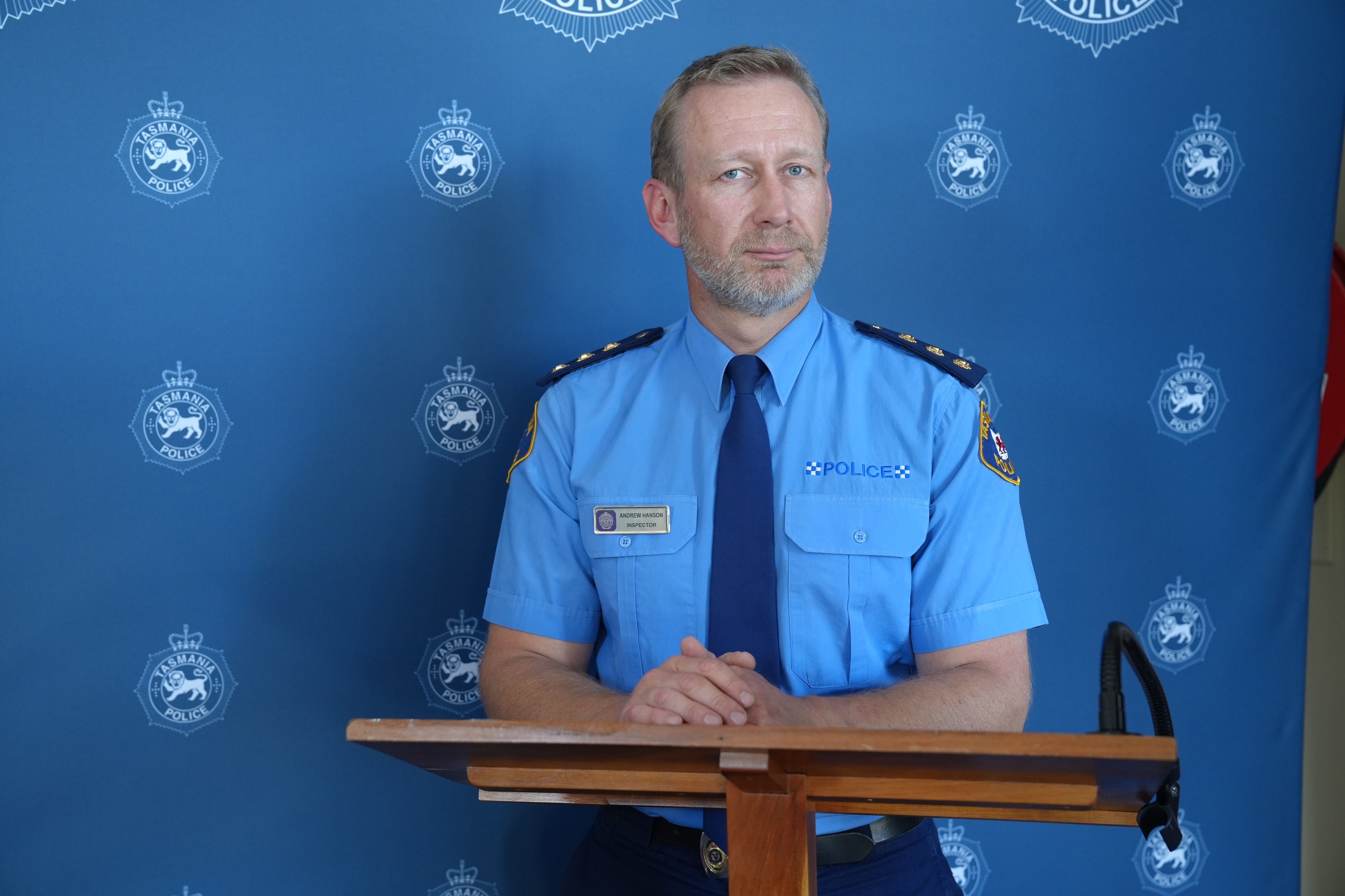 Inspector Andrew Hanson wears police uniform, stands behind a wooden lectern with and looks at the camera.