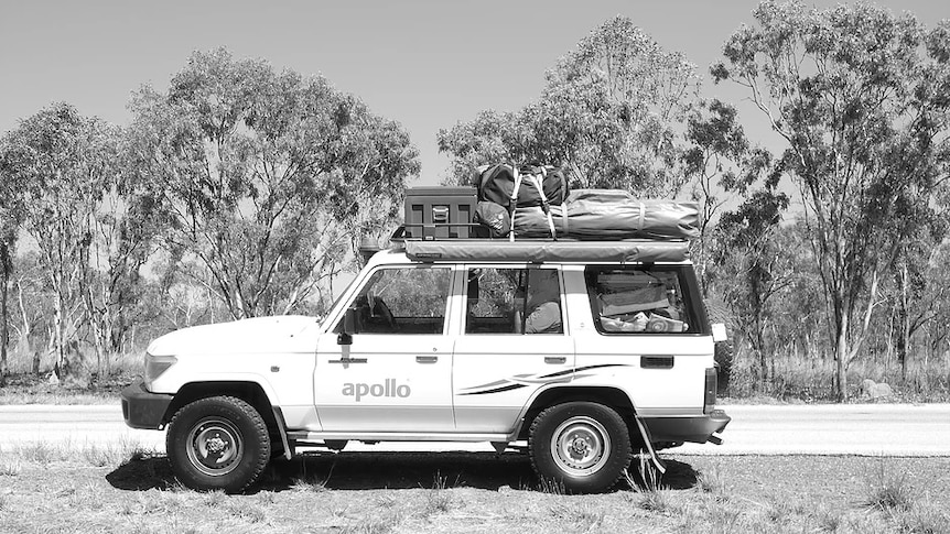 A black and white photo of a four-wheel-drive, packed with swags and camping equipment.