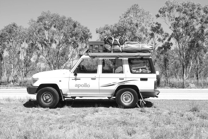 A black and white photo of a four-wheel-drive, packed with swags and camping equipment.