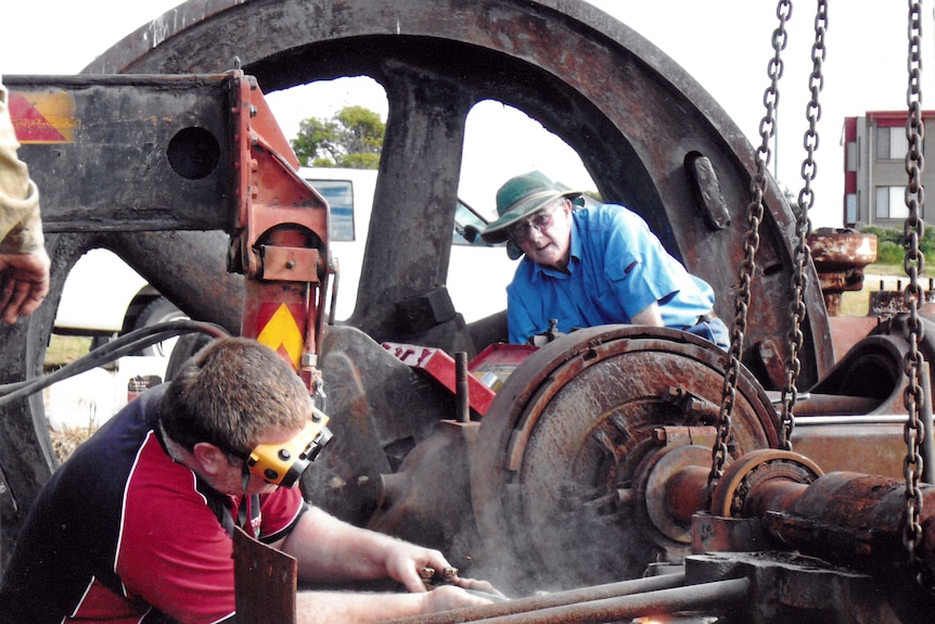 Two men working on an old and rusty machine.