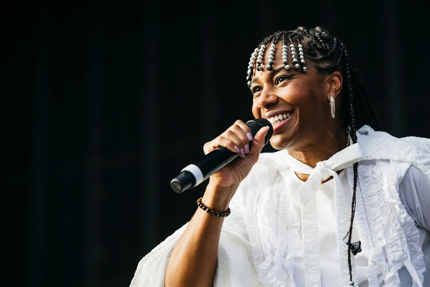 Woman wearing white smiles while singing into mic