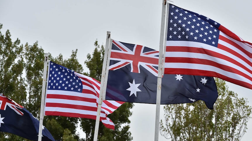 Four Australian and US flags are seen hoisted against a blue sky.