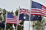 Four Australian and US flags are seen hoisted against a blue sky.