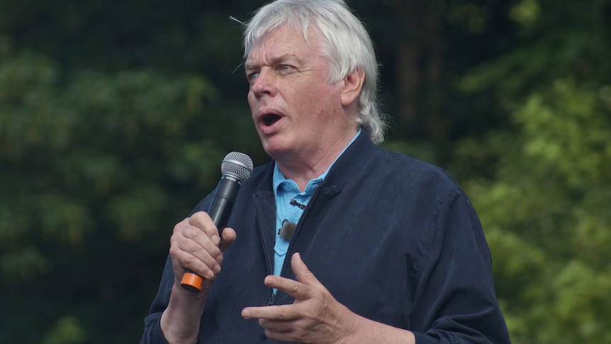 British author David Icke holds a microphone while speaking at an outdoor event