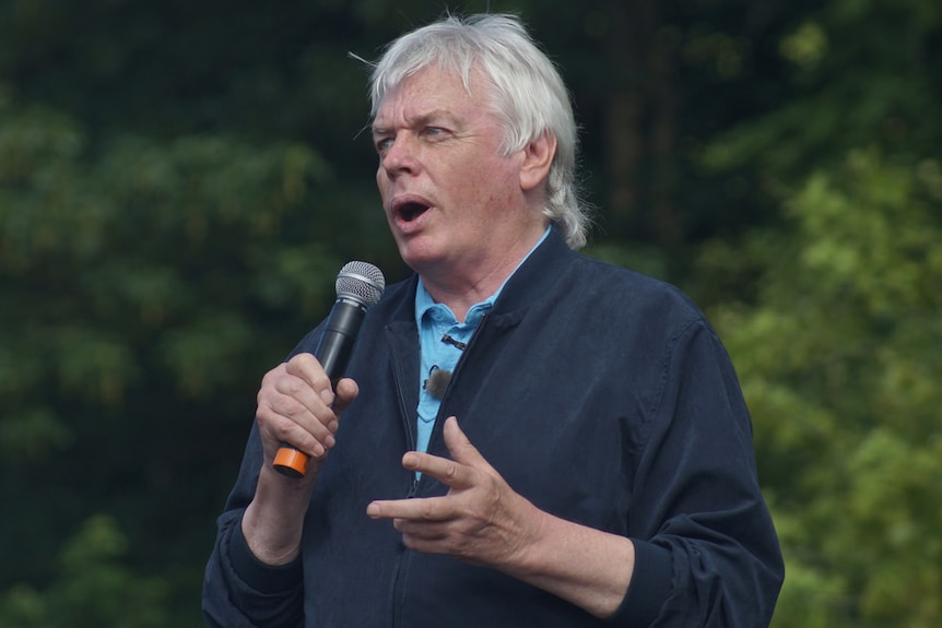 British author David Icke holds a microphone while speaking at an outdoor event