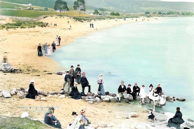 People in old-fashioned clothes sit on the beach