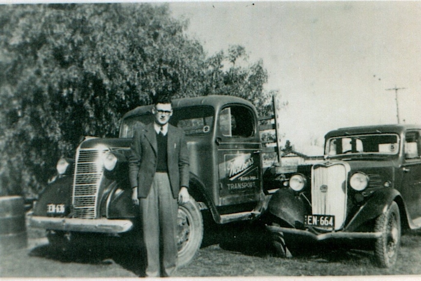 A man stands infront of an old truck in a black and white photograph 