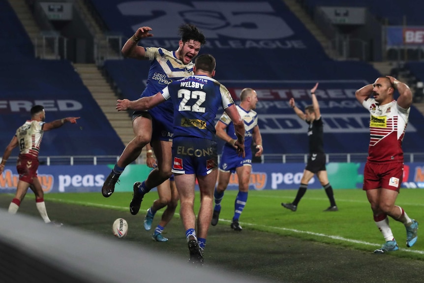 A Super League player leaps to congratulate the winning tryscorer as defenders look dejected.