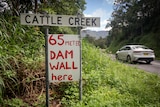 A car drives past a sign that says '65 meter dam wall here'