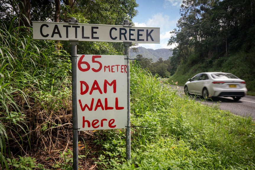 A car drives past a sign that says '65 meter dam wall here'