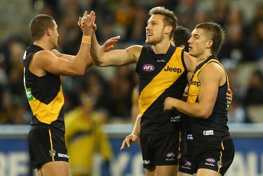 Luke McGuane is surrounded by team-mates after kicking another for Richmond against Essendon.