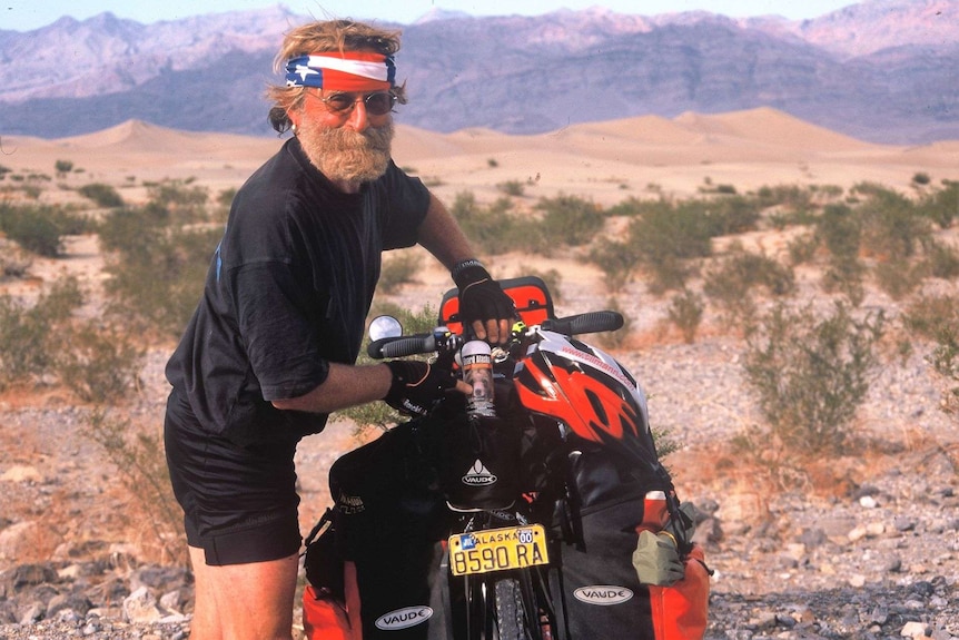 Man with American flag bandanna with a packed up bicycle and can of bear spray