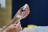 Two hands holding a COVID vaccine and syringe.