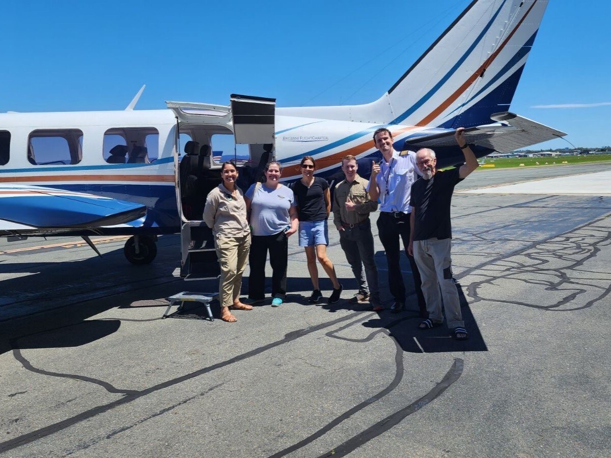 Six people are standing out the front of a small plane on a runway.