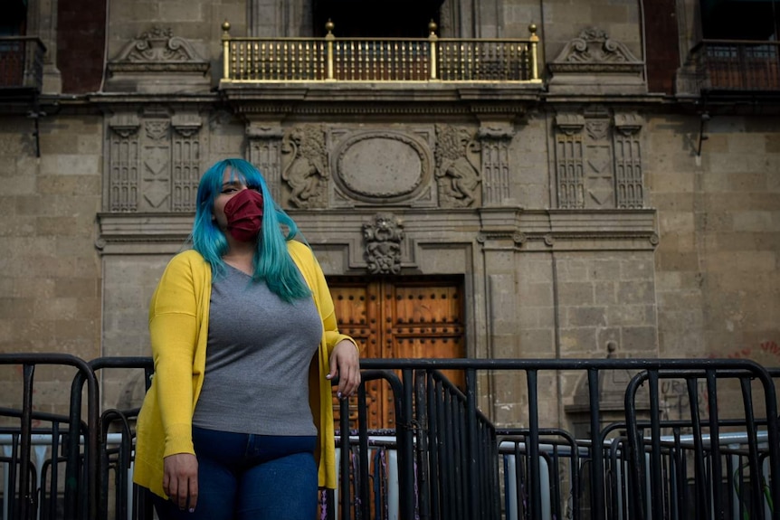 A woman with blue hair leans on a barricade outside a palace