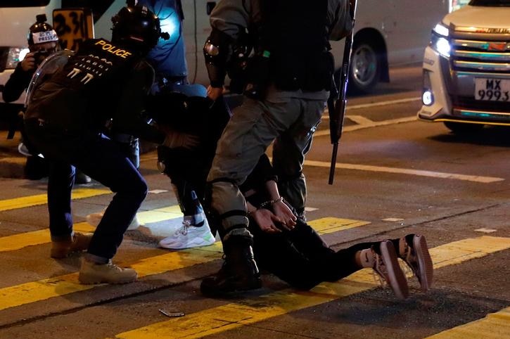Police in riot gear are arresting an anti-government protester as he is laying on the ground.