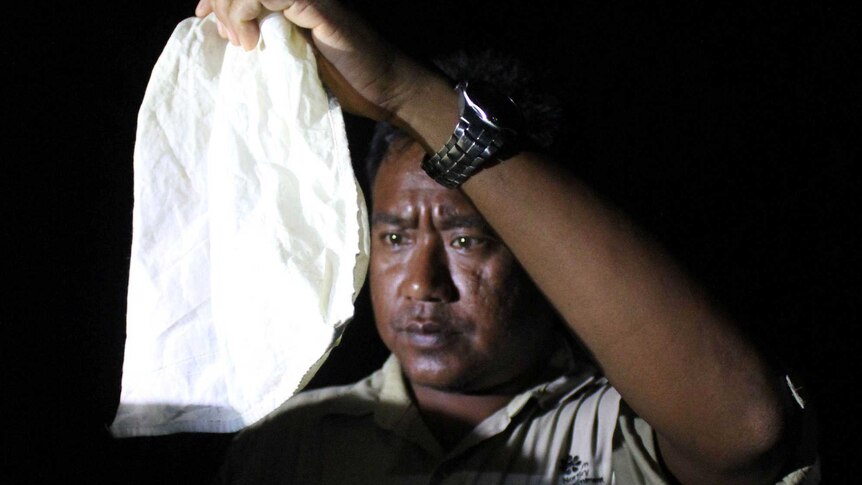 A man on a dark night holding a hessian bag up to his face.