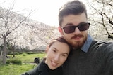 A couple pose in front of Japanese cherry blossoms.
