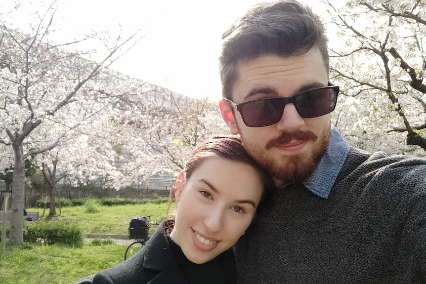 A couple pose in front of Japanese cherry blossoms.