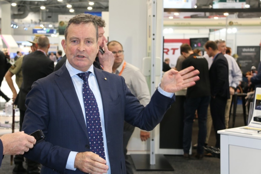 A man in a suit at a conference gestures with his hand.