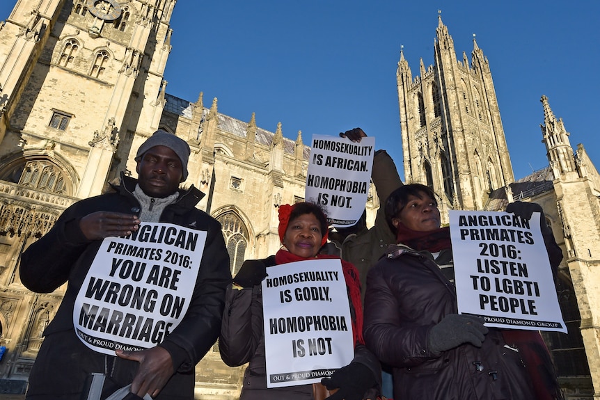 Four protesters hold signs outside the Canterbury Cathedral, saying things like 'Homosexuality is godly, homophobia is not'