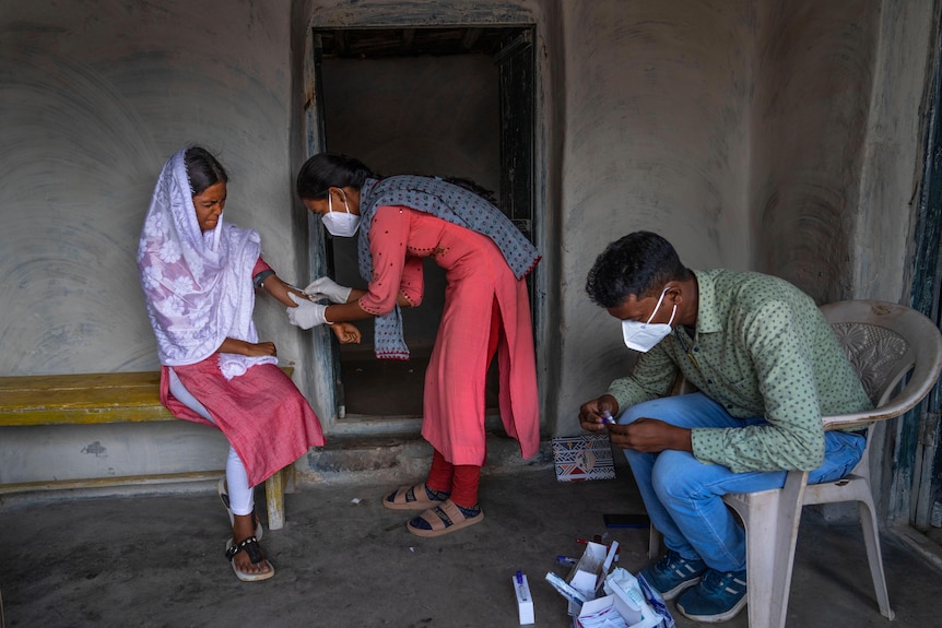Nandini Kanwar a nurse with the nonprofit Sangwari, takes a blood sample from a patient as another patient sits nearby