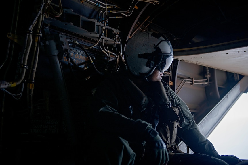 A soldier in a helmet looking out the back door of a military aircraft