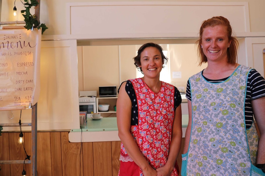 Two women on right of picture standing in front of serving window with menu on ladder on left