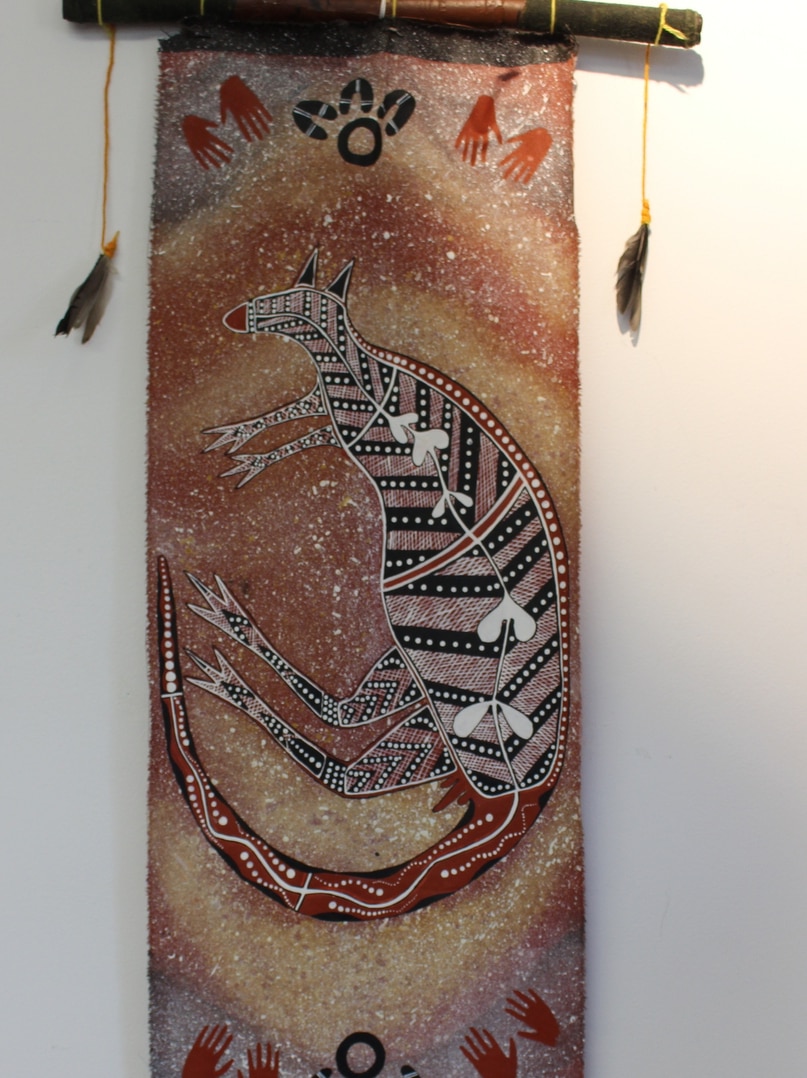 An Aboriginal painting of a stylised kangaroo with hands reaching toward it.