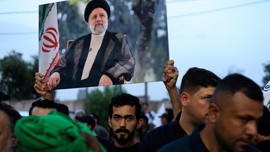 A man in a crowd holds up a large portrait of Ebrahim Raisi