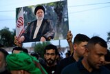 A man in a crowd holds up a large portrait of Ebrahim Raisi