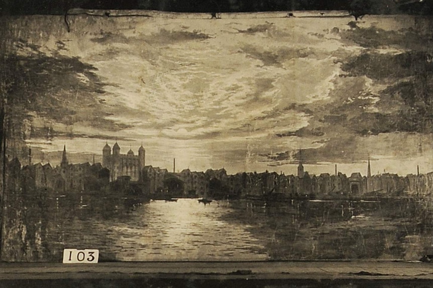 A black and white photograph of a painted backdrop depicting a body of water with a dense, old town behind.