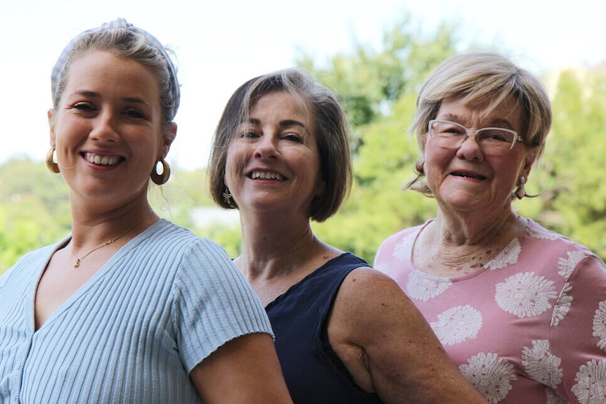 Three women stand in line, smiling together.