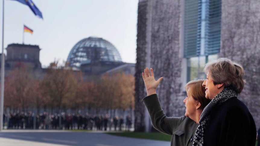 With the German Reichstag in the distance, Angela Merkel and Theresa May look up at a large EU flag in an empty square.