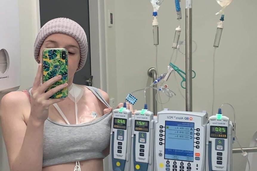 Lauren Anderson takes a selfie in front of a mirror while hooked up to machines at a hospital.