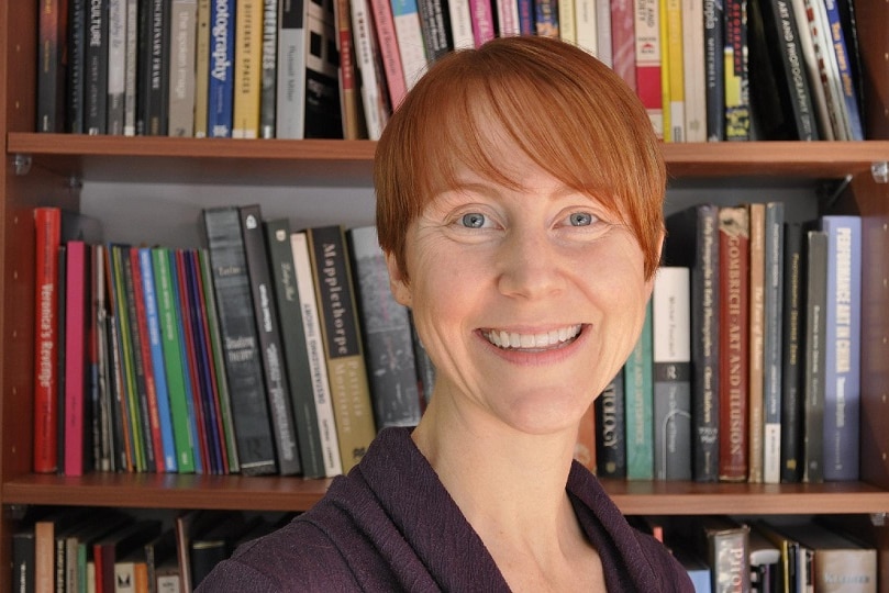 A university researcher stands in front of a library and smiles to the camera