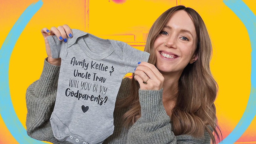 Kellie holds up a baby onesie that asks her to be a godparent