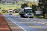 Two trucks driving along the Great Northern Highway, paddocks in the background.