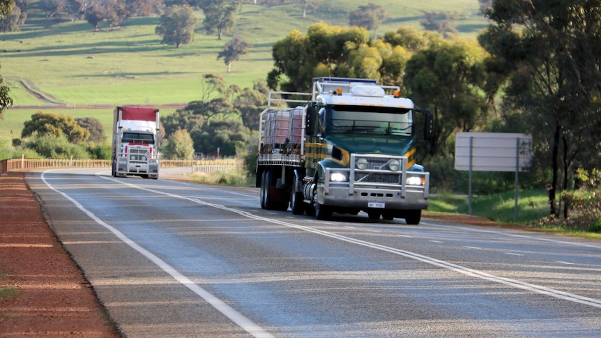 Two trucks driving along the Great Northern Highway, paddocks in the background.