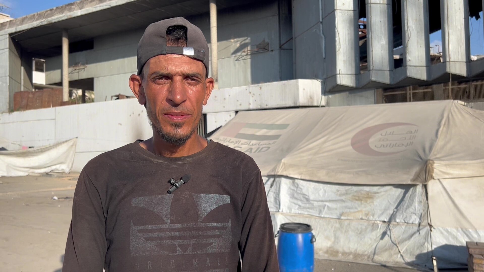 A man wearing a hat stands in front of a tent