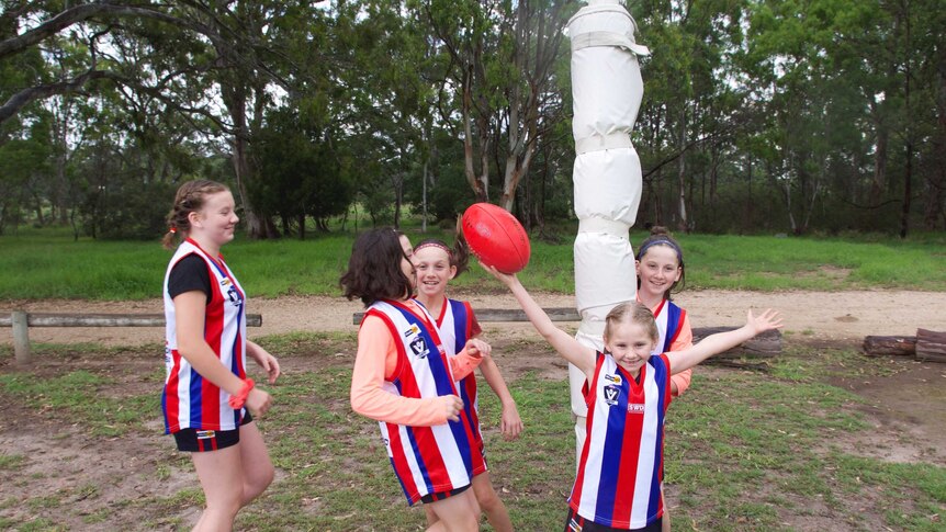 Five sisters playing footy together, wearing red, blue and white striped football jumper.