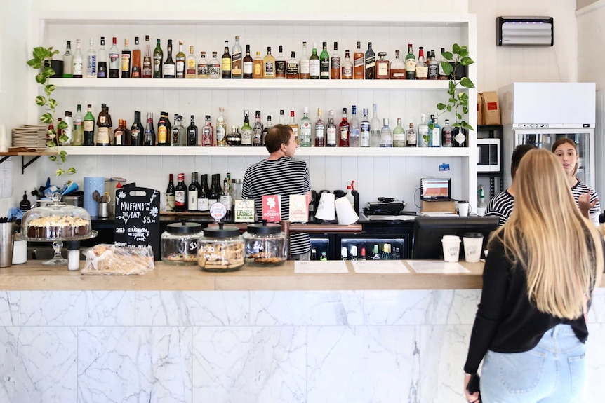 A well lit, well stocked, well staffed  bar and front counter at a restaurant.