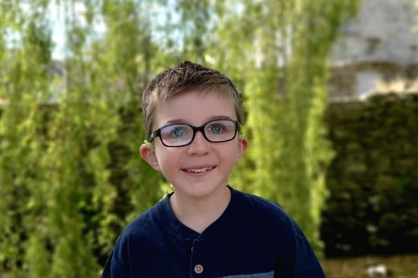 Nine year old Toby Jamieson sitting in front of greenery, wearing glasses.