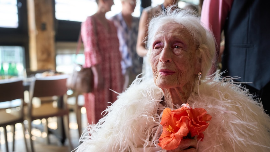 An older woman, Eileen Kramer, wears a ballgown while sitting in a wheelchair