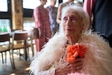 An older woman, Eileen Kramer, wears a ballgown while sitting in a wheelchair